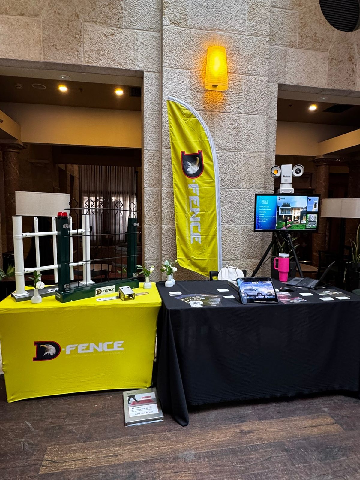 D-FENCE 展台：传感器围栏样品、压力感应带、PTZ 摄像机，以及平板电脑上展示的 NOA