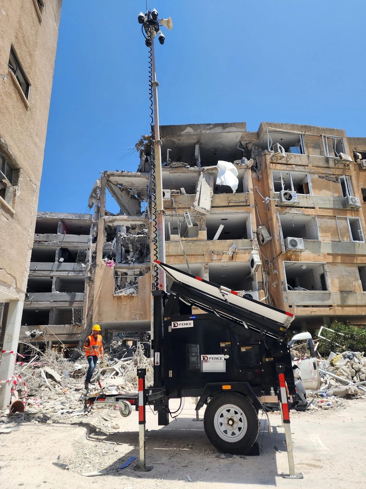 AI-EYE IN THE SKY solar trailer with its camera mast raised beside a damaged apartment block