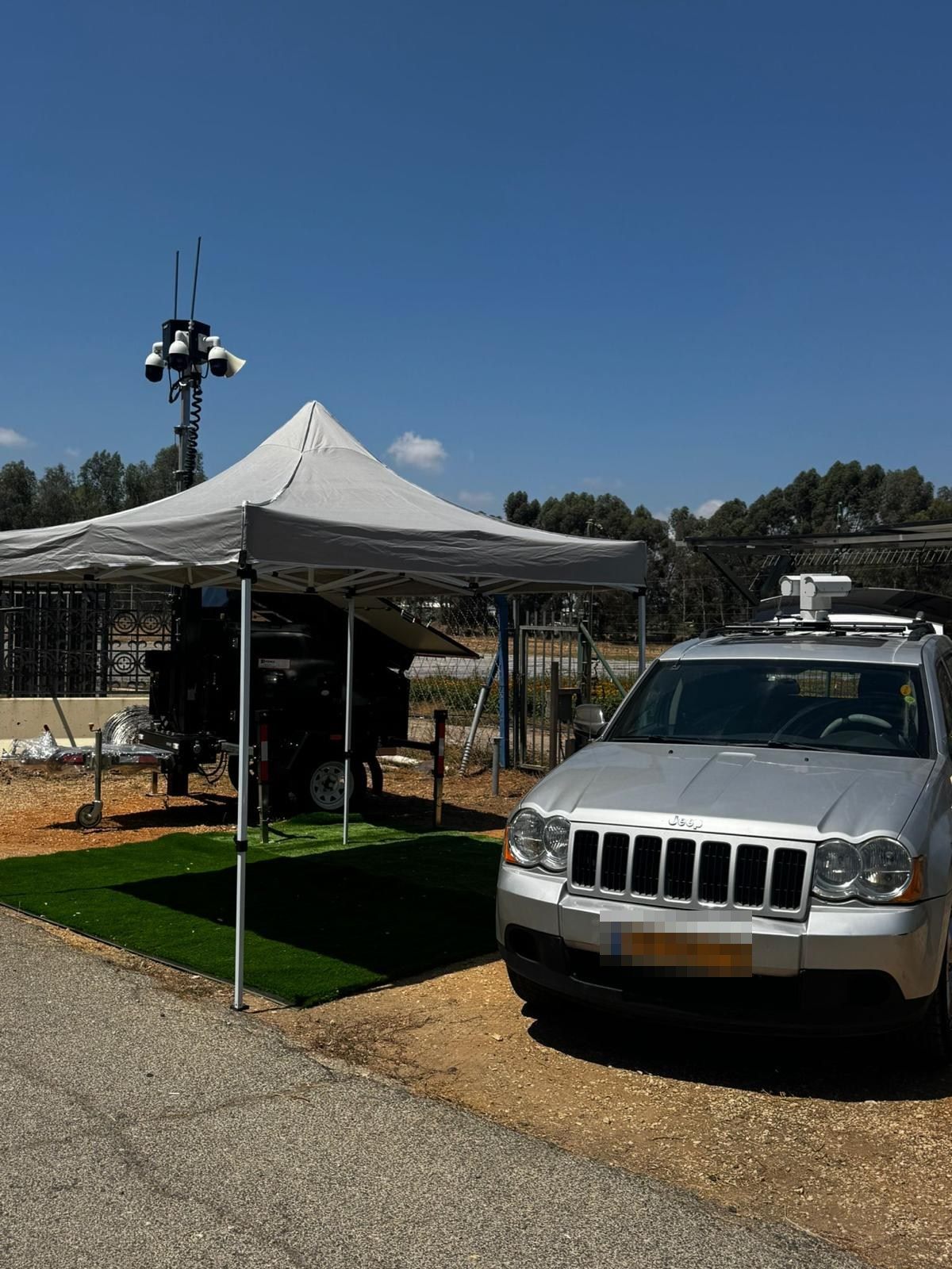 AI-EYE IN THE SKY trailer with its mast raised under a canopy at a test site, a patrol SUV with a NOA head on its roof in front