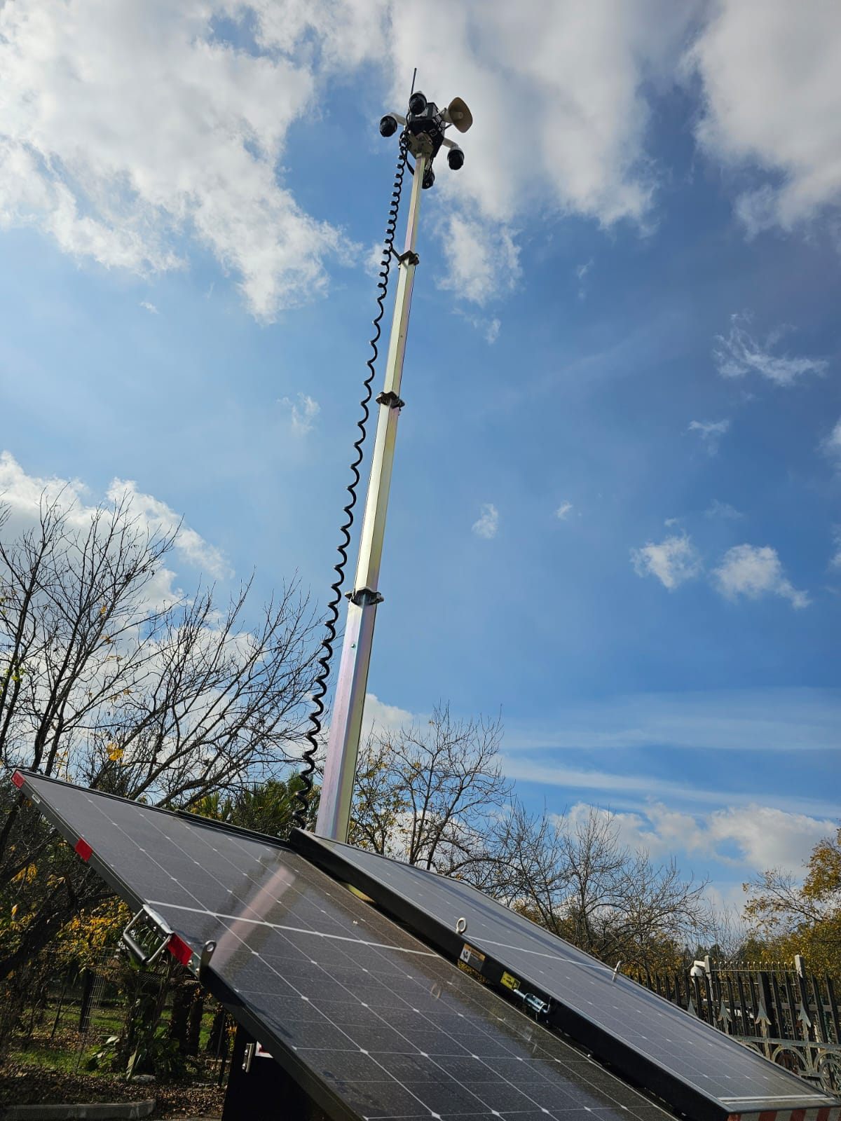 Camera head with PTZ domes and a loudspeaker on top of the telescopic mast, seen from below above the solar panels