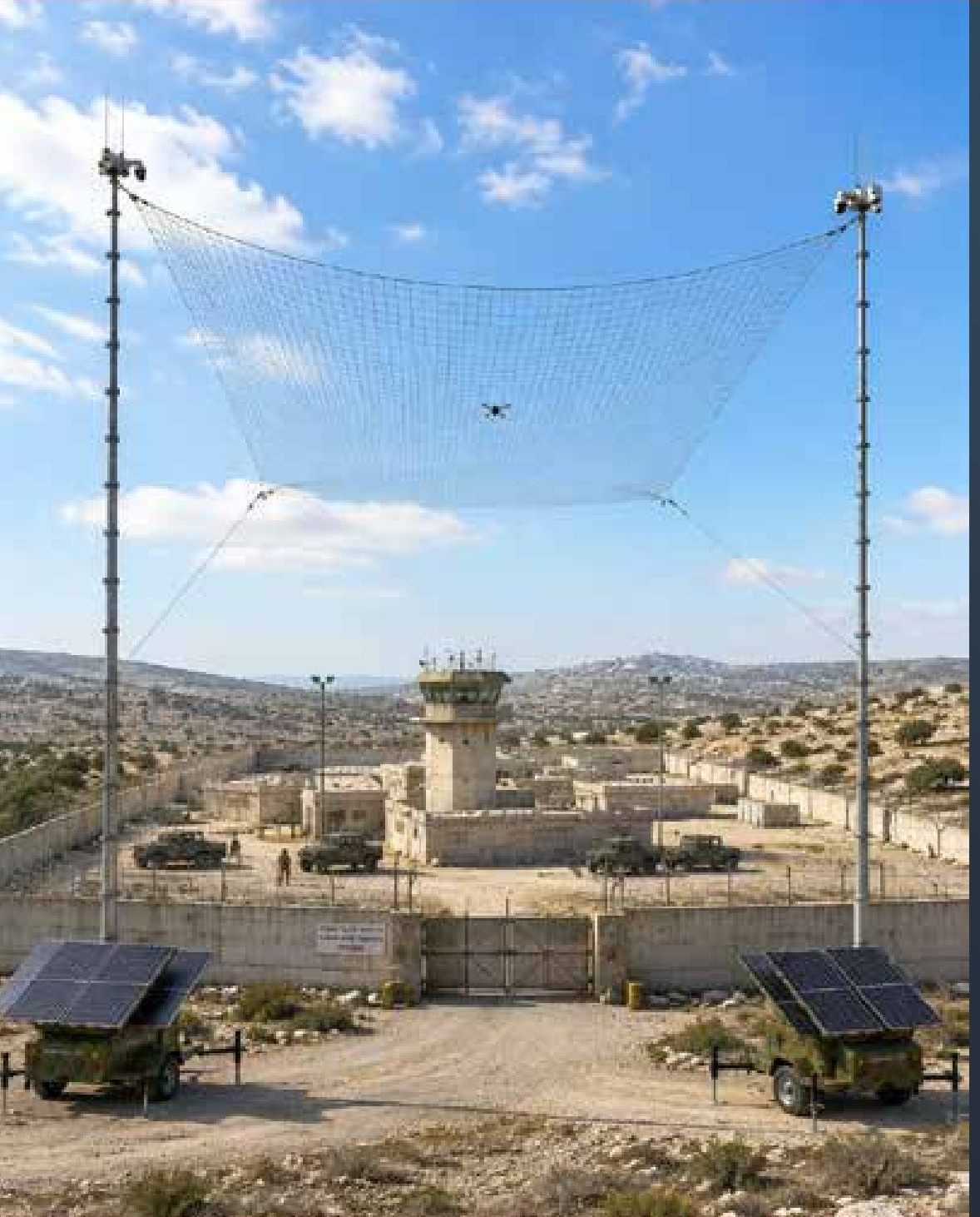 Horizontal anti-drone net held by two camouflaged solar trailers over the gate of a desert base with a watchtower (concept render)