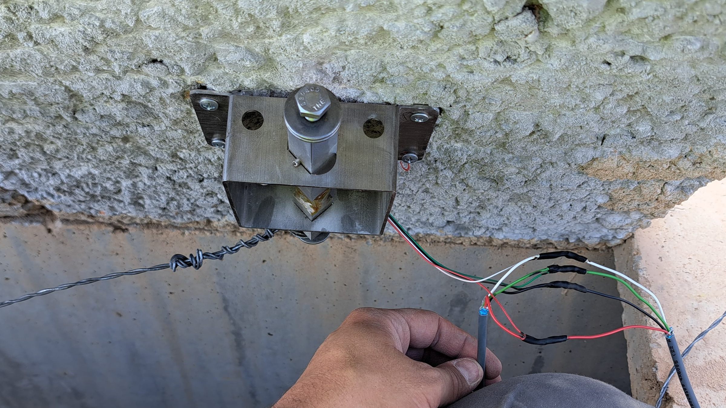 Installer wiring a D-FENCE sensor mounted under the concrete cover of a railway cable trough; a tensioned wire runs along the trough