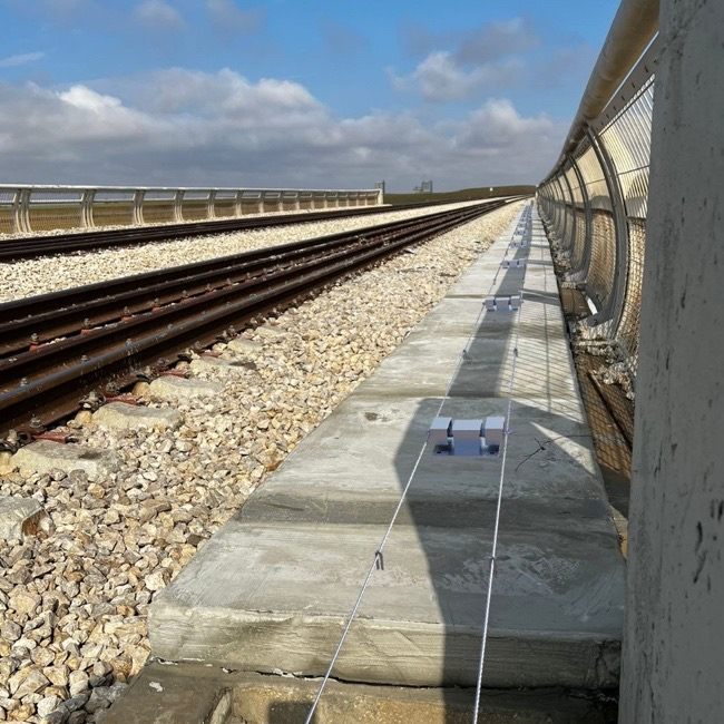 Railway bridge with a concrete cable trough beside the track; D-FENCE sensor units and wires sit on the cover slabs