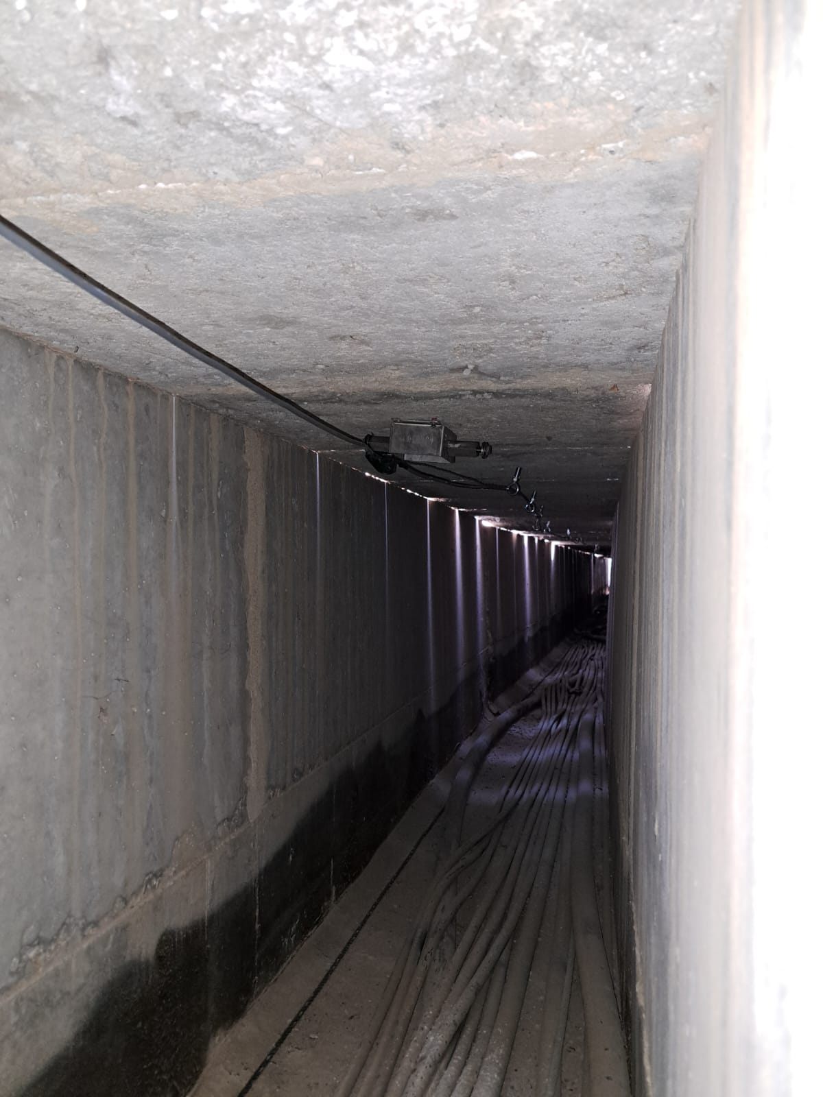 View along the inside of a cable trough: a D-FENCE sensor and its tensioned wire run under the cover, above the communication cables