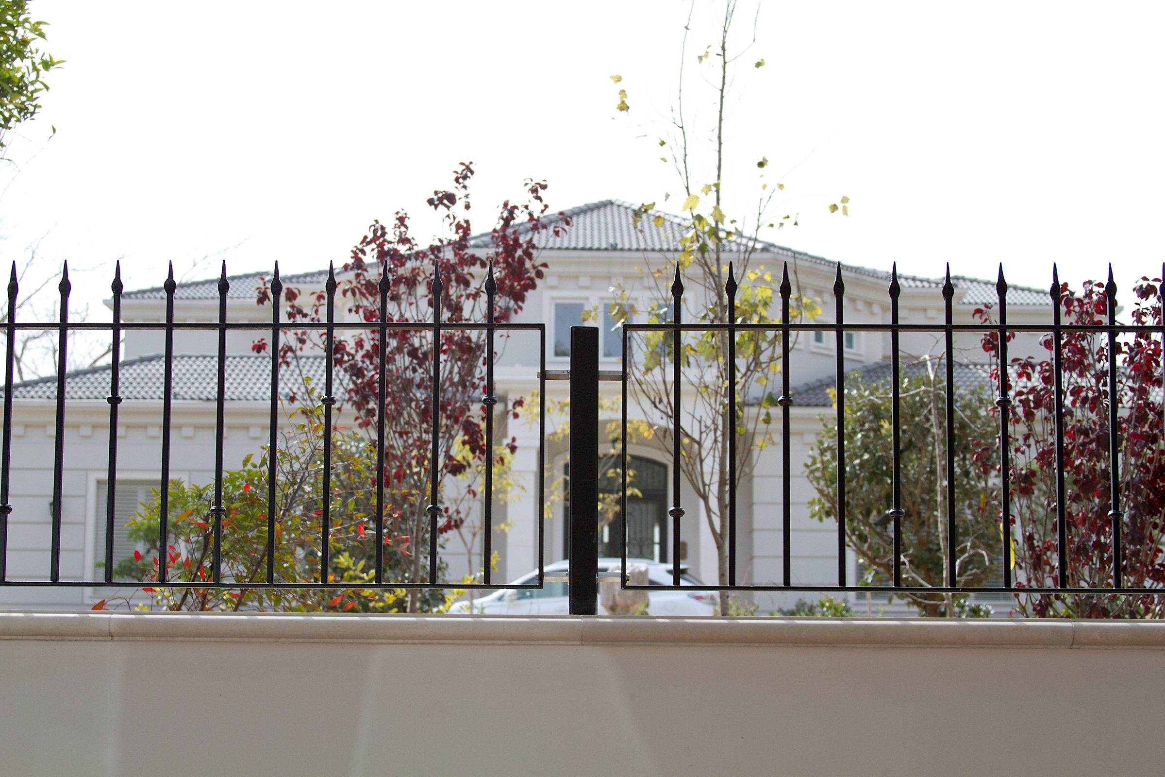 Black ornamental fence with a D-Corative sensor post on a cream wall in front of a villa