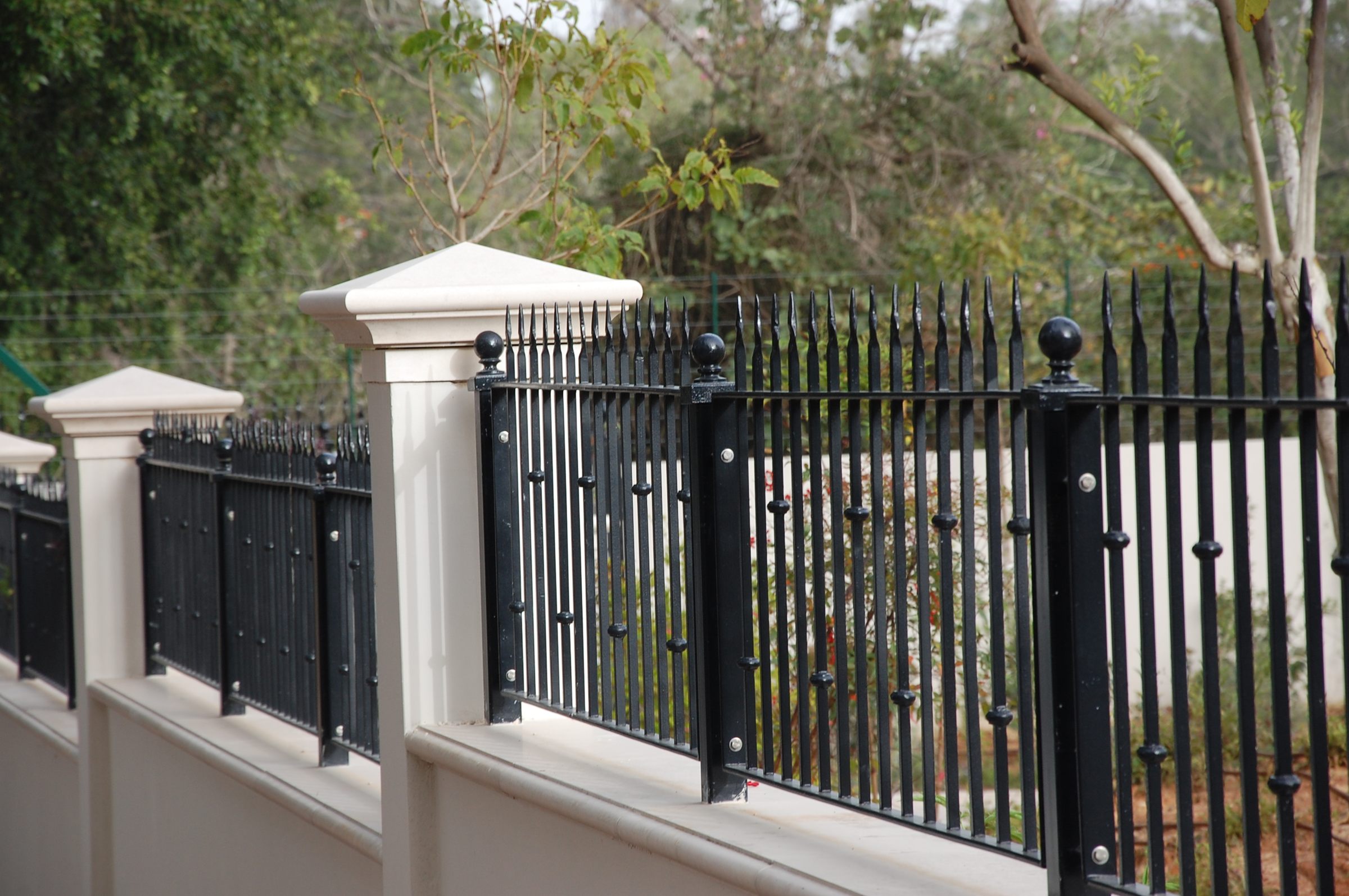Black spear-top ornamental fence with D-Corative sensor posts between stone pillars on a garden wall