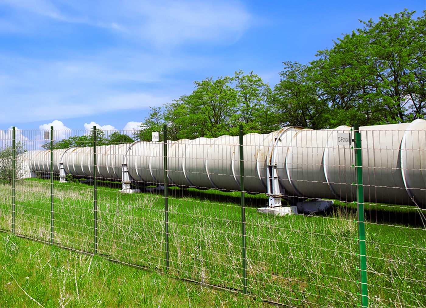 Render: field fence with a green sensor post alongside an above-ground pipeline