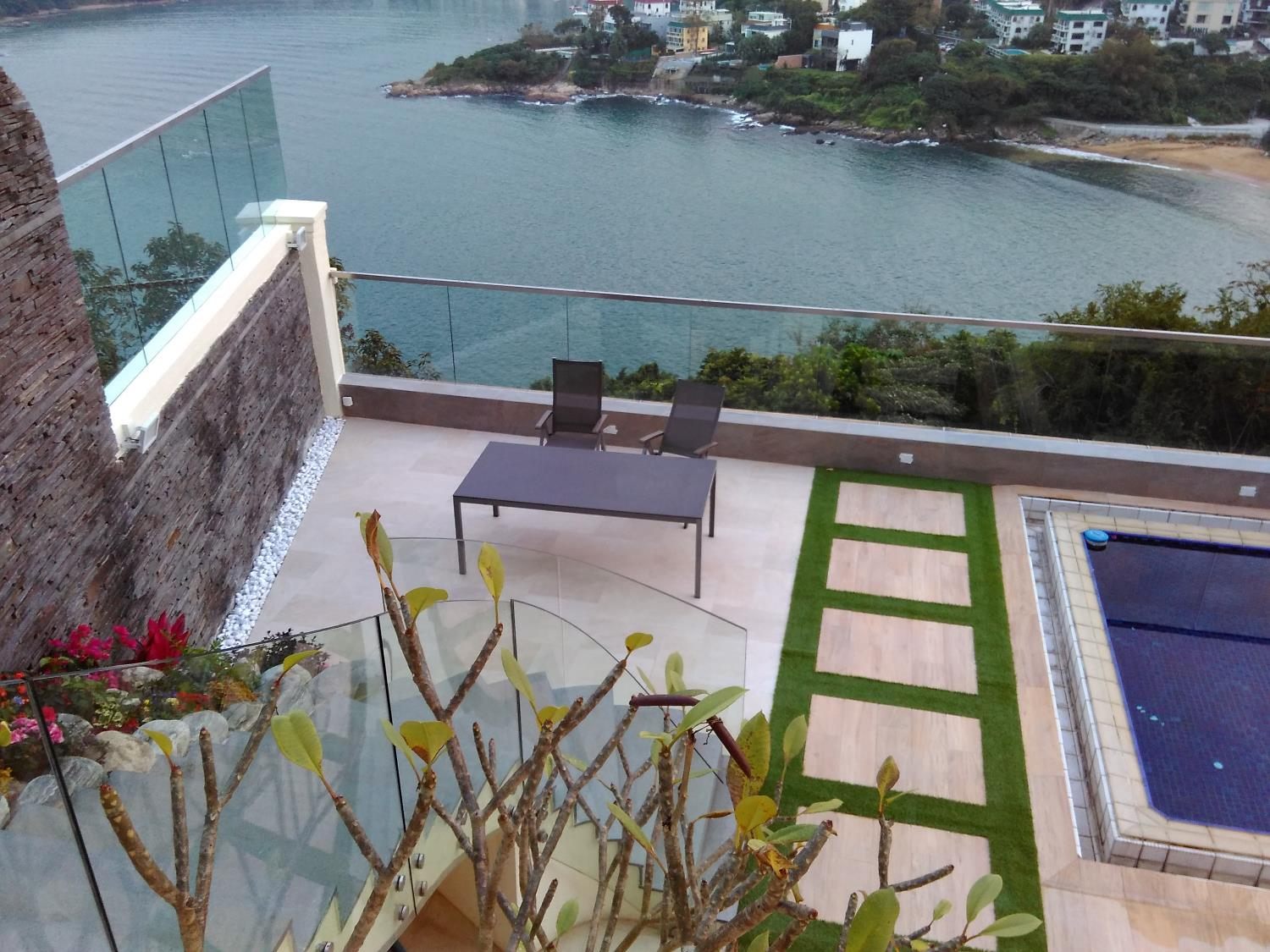 Seaside villa terrace with a pool and lawn strips, enclosed by frameless glass balustrades on two levels