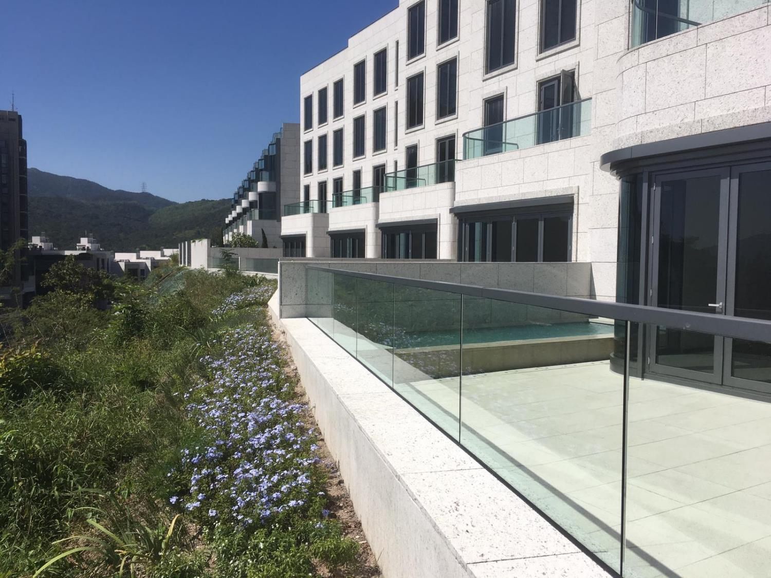 Ground-floor terraces of a stone-clad residential building, edged by a glass balustrade with a dark capping above a planted slope