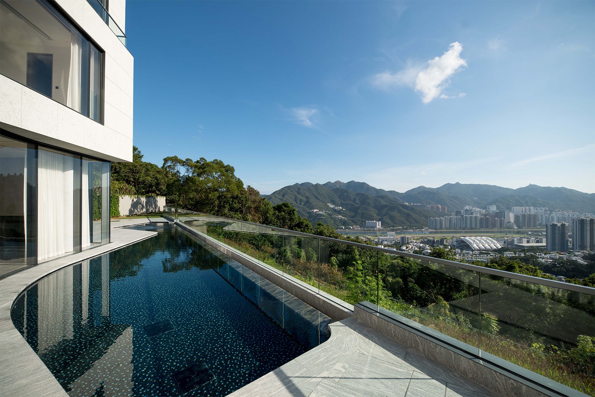 Frameless glass balustrade with a metal capping along an infinity pool, mountains and city below