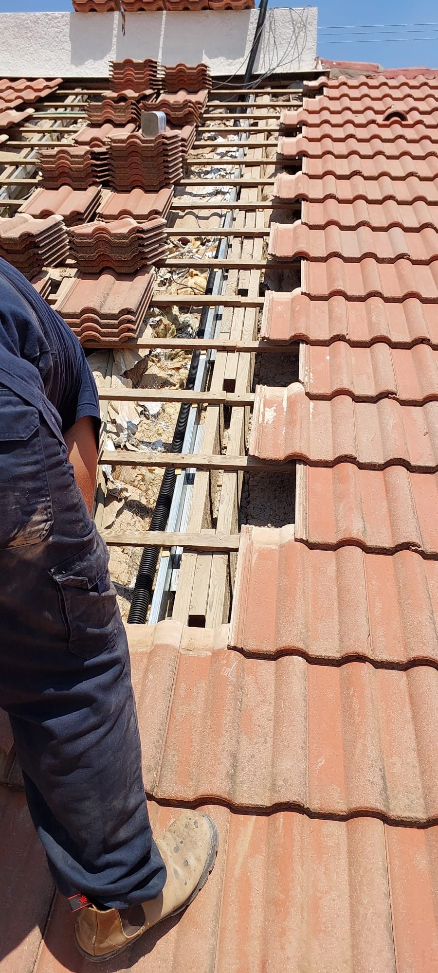 Installation photo: a row of roof tiles removed to show D-Roof sensor rails laid on the battens, with the installer standing beside them