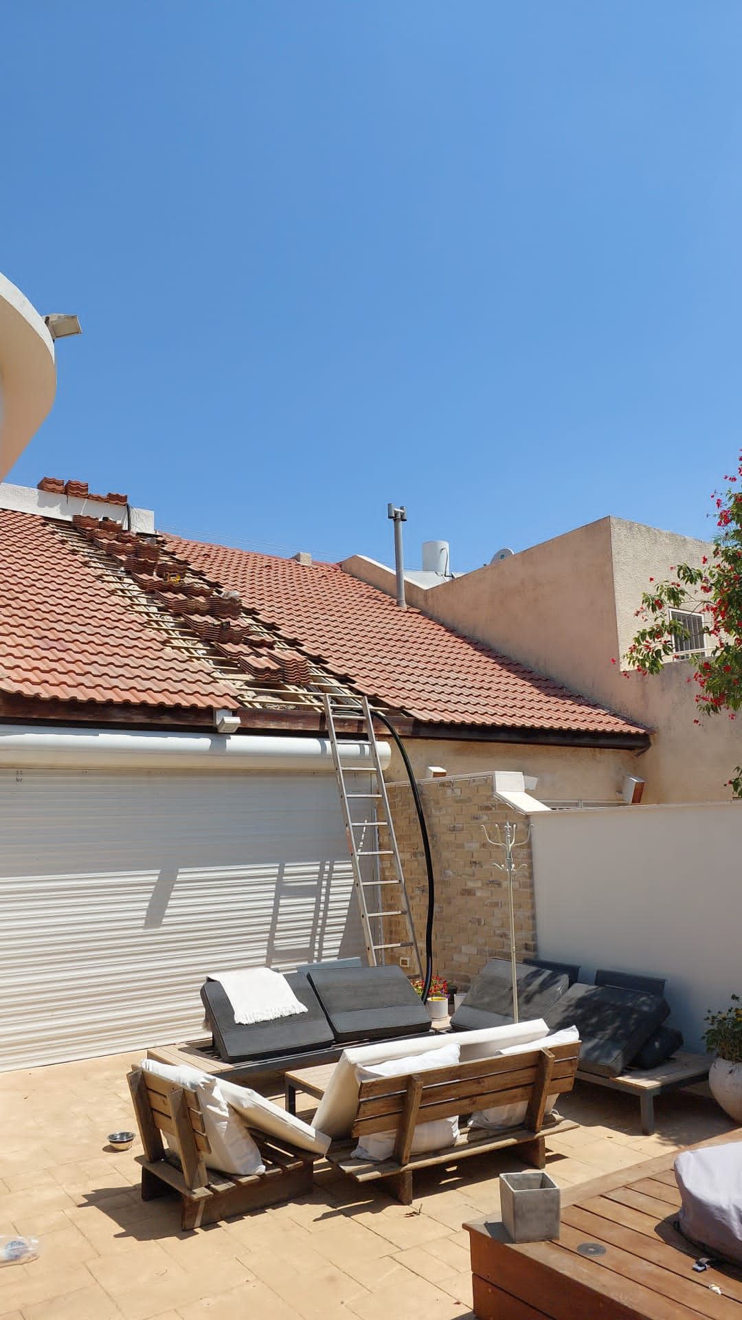 Tiled roof of a private house during installation: a line of tiles lifted along the roof slope, a ladder and cable leading down to the patio