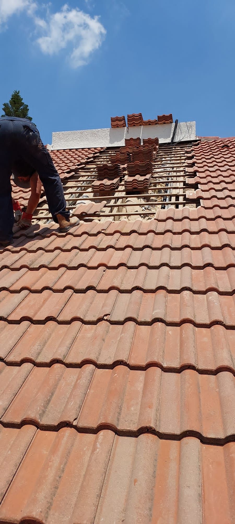 Installer kneeling on a tiled roof, tiles stacked beside the open strip where the D-Roof sensors are laid