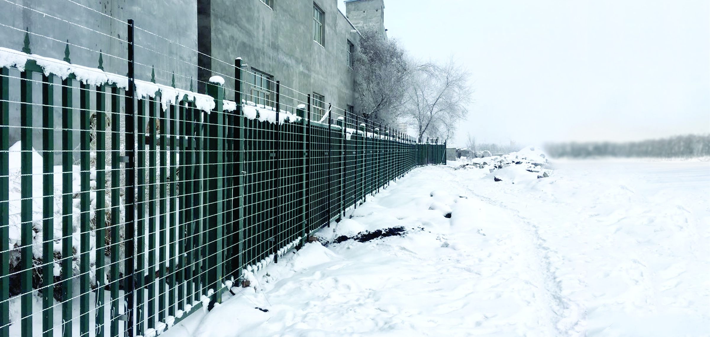 Green palisade fence topped with taut wires along the outer perimeter of a military camp in deep snow