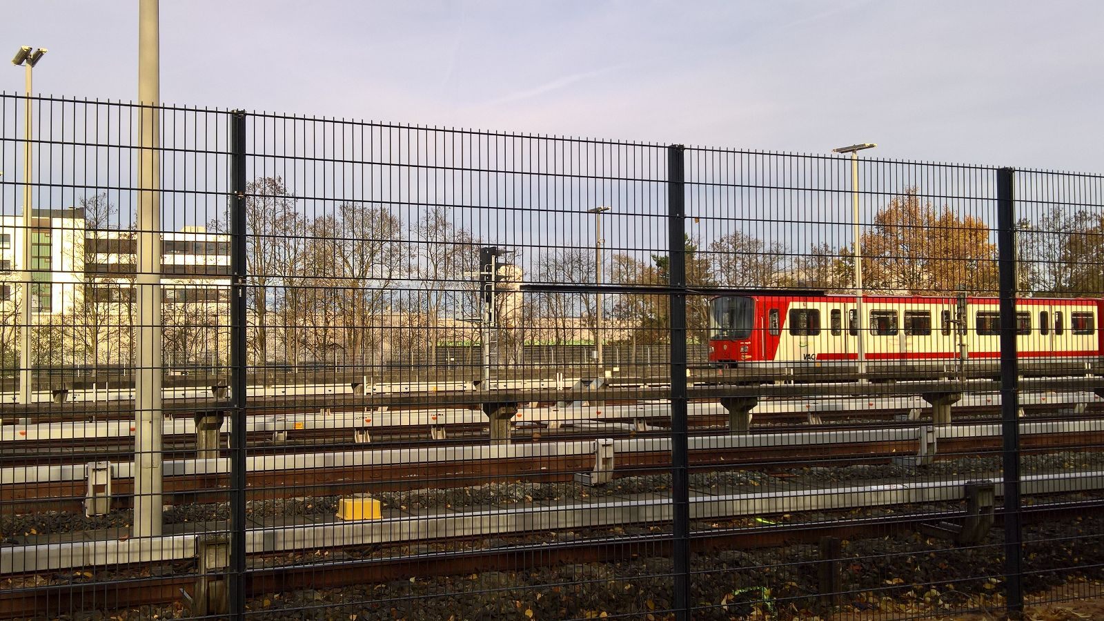Regional train passing behind a double-wire welded-mesh fence at a rail yard