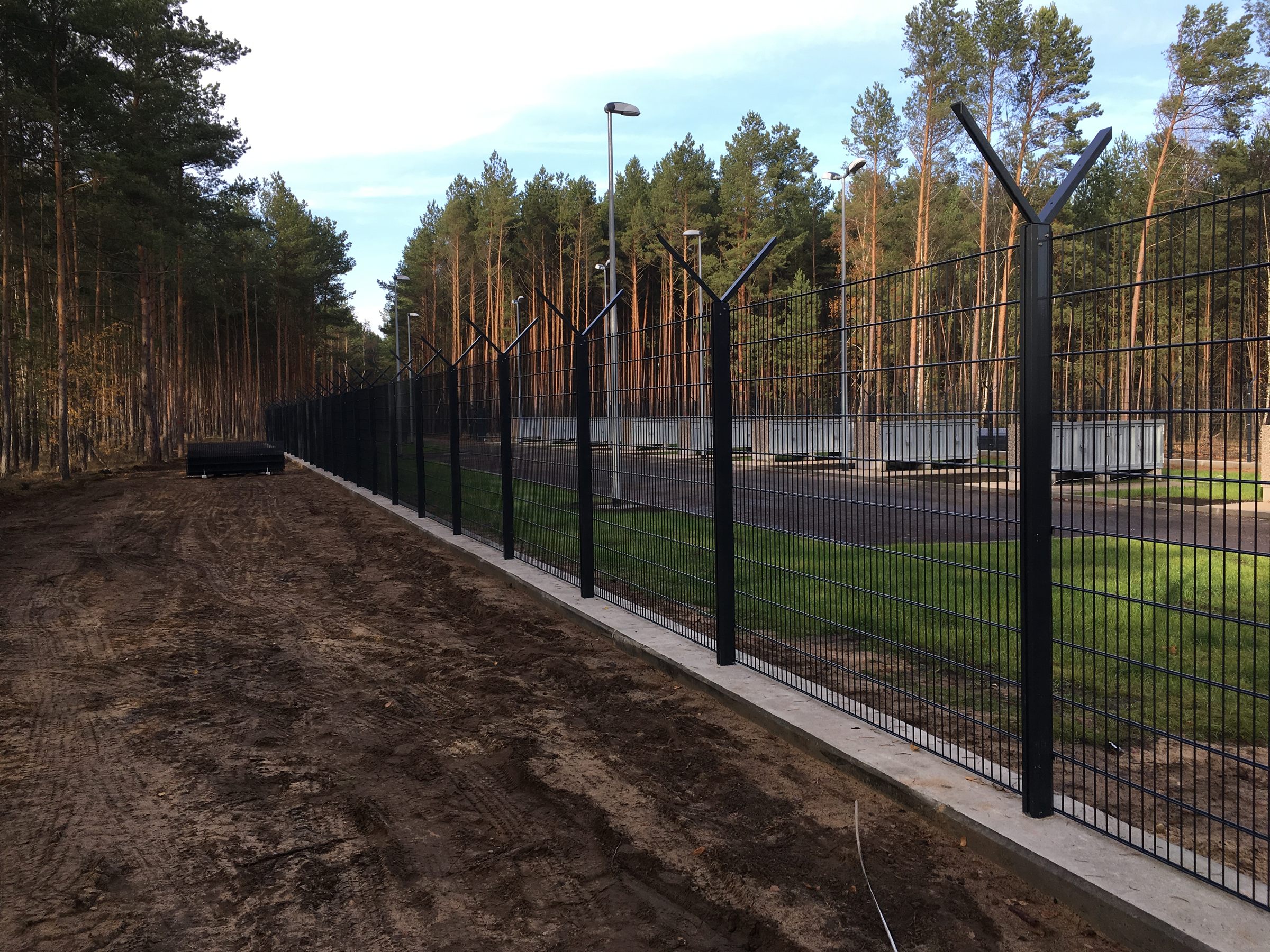 A welded-mesh fence on D-FENCE sensor posts along a forest road