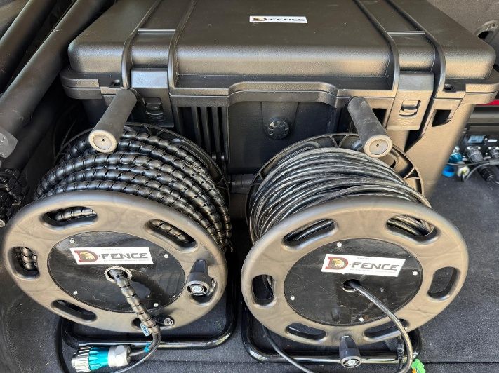 Two D-FENCE cable reels in front of the NOA case in a vehicle trunk